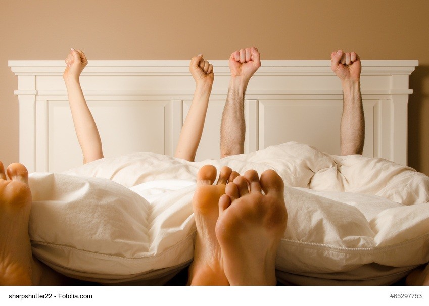 Zwei Menschen liegen morgens im Bett und strecken ihre Hände an die Decke
